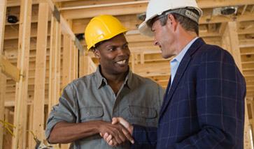 two men in hard hats on construction site shaking hands